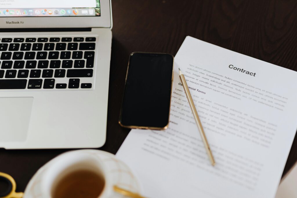 a laptop and a paper document, ready to be signed with a pen