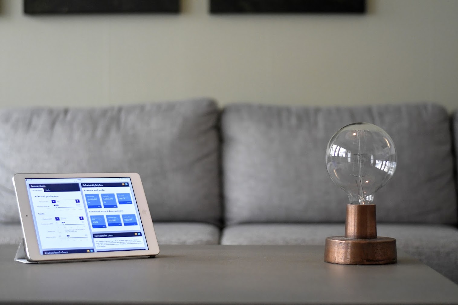 Tablet showing a Molnify web app next to a decorative lamp on a coffee table in front of a grey sofa.